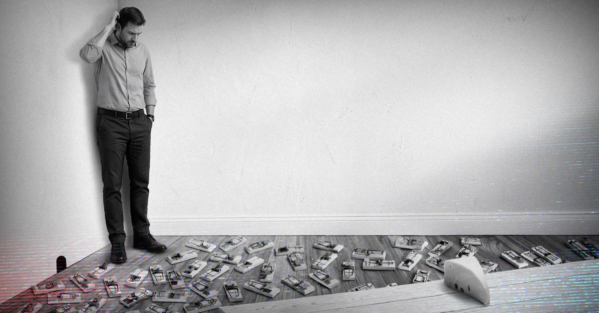 Man in business attire standing confused by a floor filled with numerous mousetraps in a minimalist room.